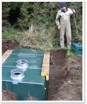 Green fibreglass tank with inspection hatches being buried, representative of the 4000 litre septic tank