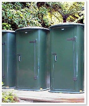Three dark green NFP wilderness toilets standing side by side in native bush