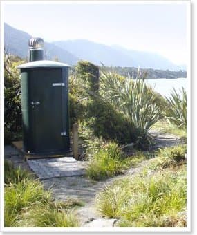 Green NFP toilet with a super vent beside a coastal track, flax and hills behind